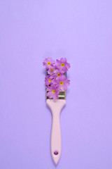 Creative concept. Paintbrush with Purple flower on pastel purple background. Minimal nature composition with copy space.Flat lay, top view.