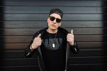 American hipster young man in sunglasses in a fashionable leather black jacket in a stylish...