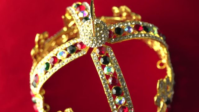 Gold crown with luxury color jewels and diamonds. With reflection and lights sparks. Slow rotation on the red royal color surface. 4k, uhd. Focus on the top.