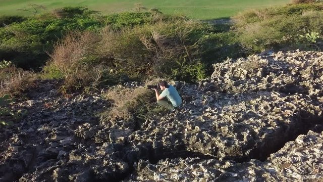 A wildlife photographer hiding behind cactus bushes to get photos of wild goats in Aruba.