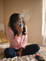 african american woman smoking marijuana joint while sitting on bed at home © Joshua Resnick