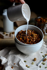 tasty homemade oats granola with nuts and berries in white ceramic bowl served with coconut milk on the wood table for breakfast early in the morning