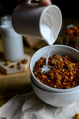tasty homemade oats granola with nuts and berries in white ceramic bowl served with coconut milk on the wood table for breakfast early in the morning