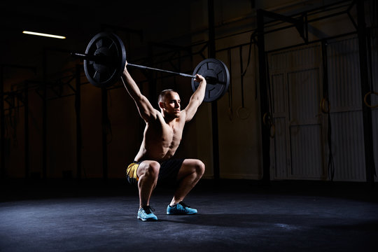 Athletic man training squats with barbells over head - Powered by Adobe