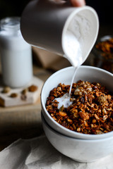 tasty homemade oats granola with nuts and berries in white ceramic bowl served with coconut milk on the wood table for breakfast early in the morning