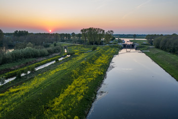 A canal with dike / shore with grass and yellow land crest during sunset near Waalwijk, Noord Brabant, Netherlands.