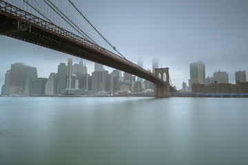 Financial District and Brooklyn bridge from East River on a foggy day with long exposure