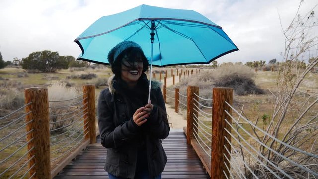 A beautiful young woman smiling and laughing in the rain with a blue umbrella in the storm and bad weather SLOW MOTION.
