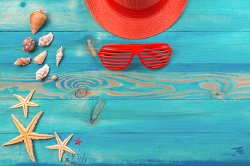 Top view on living coral color hat, louvered sunglasses, seashells and starfish on blue painted vintage wooden texture. Flat lay, copy space.