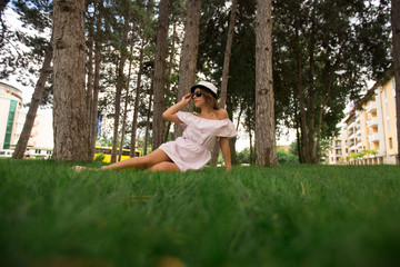 Naklejka na ściany i meble Beautiful girl in dress and hat in the park. Green grass and sunny. Background of trees