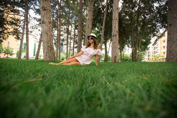 Beautiful girl in dress and hat in the park. Green grass and sunny. Background of trees