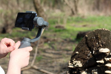 A young man videotaping on a smartphone. Uses gimbal to get smooth footage. Closely watching the movie shooting.