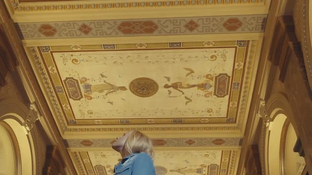 View looking up at a woman notices the ceiling art among golden archways, 60 fps.