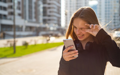 Outdoor portrait of young teenager brunette girl with long hair. girl on city in black dress looking on the smart phone walking in the street in a sunny day