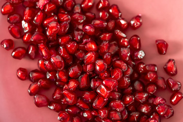 Beautiful blurry backdrop with red seeds pomegranate on a pink plate. Macro image of red grains. Soft focus. Healthy concept.