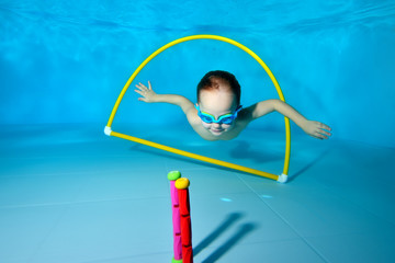 A little boy is engaged in scuba diving in the pool and dives for toys through the Hoop at the bottom. Portrait. Underwater photography. Horizontal orientation of the image © alexbard