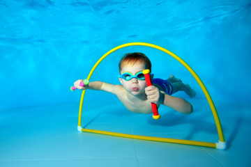 A little boy dives and pulls toys from the bottom of the pool and poses with them on camera....