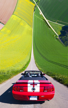 Red cabriolet in yellow and green fields