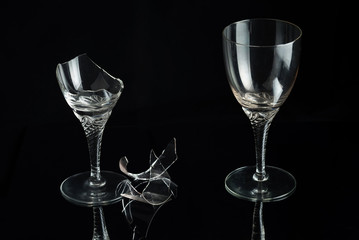 Two crystal wine glass and shattered glass on a black mirror background. New and broken.
