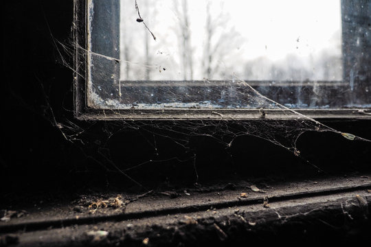 A dirty, dark window in a dark room with spider webs and a dirty window sill