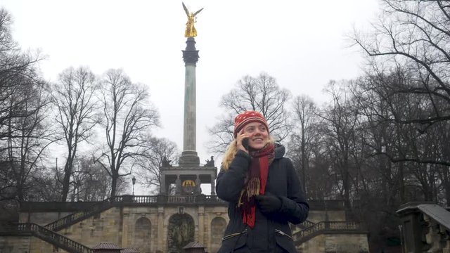 Close Up: Blonde woman making a phone call in front of the friedensengel in Munich.