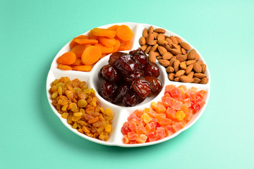Mix of dried fruits and nuts on a white plate. Apricot, almond, raisin, dates fruit. On a green background. Space for text or design.