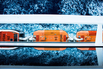 Orange lifeboats on board of huge cruise ship with foamed sea water on the background. Seascape....