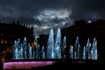 Illuminated fountain on a central square at night with blue jets and pink lights with silhouettes...