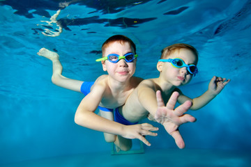 Two happy little boys are swimming, cuddling and playing underwater in the pool on a blue background. Portrait. Close up. Underwater photography. Horizontal orientation of the image