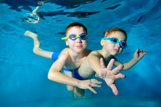 Two happy little boys are swimming, cuddling and playing underwater in the pool on a blue background. Portrait. Close up. Underwater photography. Horizontal orientation of the image