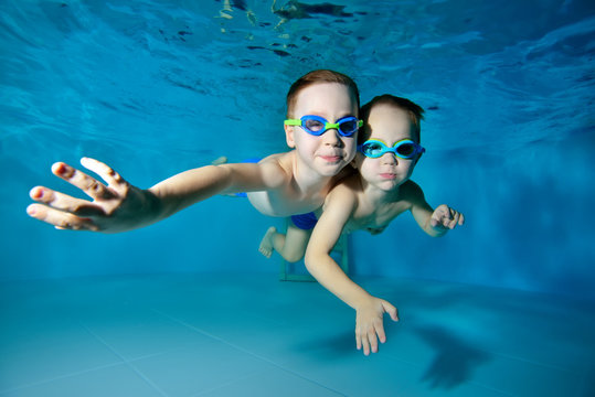 Happy kids, two little boys, swimming underwater in the pool on a blue background. They hug and pose for the camera. Portrait. Close-up. Underwater photography. Horizontal view