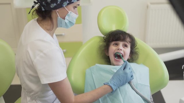 A dentist uses a suction in order to get rid off unneeded saliva from patient's mouth. The patient is a little girl who is covered with a bib/towel. The background is blurred