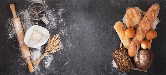 fresh bread with wheat ears, flour and kitchen utensils on dark board