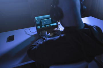 cybercrime, hacking and technology concept - male hacker in headphones with progress loading bar on laptop computer screen using virus program for cyber attack in dark room