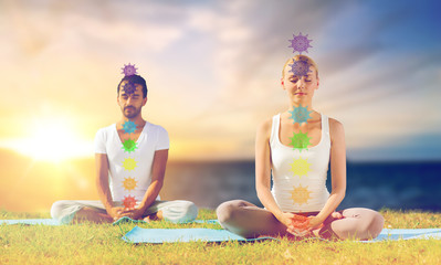 mindfulness, spirituality and outdoor yoga - couple meditating in lotus pose with seven chakra...