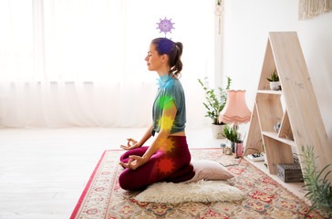 mindfulness, spirituality and healthy lifestyle concept - woman meditating in lotus pose at yoga studio with seven chakra symbols - obrazy, fototapety, plakaty