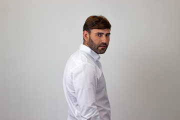 Fototapeta premium Moda portret przystojny, młody człowiek z brązowymi włosami, robiąc ciekawą twarz plecami twarzą do aparatu i patrząc w kamerę. Na białym tle