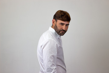 Obraz premium Fashion portrait of handsome young man with brown hair looking seductive, their back facing the camera and looking at the camera. Isolated on white background.