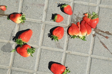 Red ripe smashed strawberries on grey concrete paving slab.