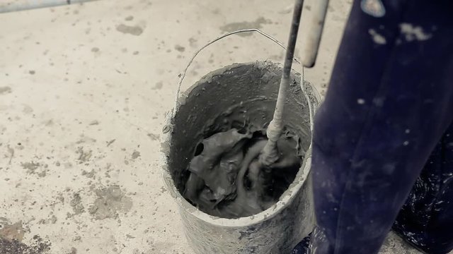 Worker mixing cement glue in a bucket with long drill.