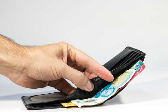 A male hand opening a leather wallet showing a five pound polymer from UK.
