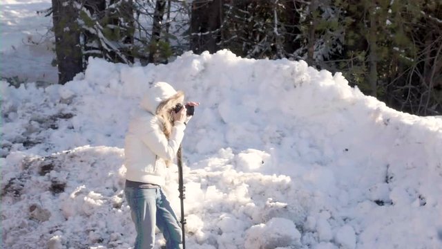 Female photographer taking images within a snowy forest scene.