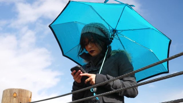 Young woman checking the weather or texting on smartphone with umbrella under blue sky with rain clouds SLOW MOTION.