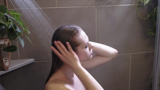 Young blond woman relaxing in shower, hot water flowing over head