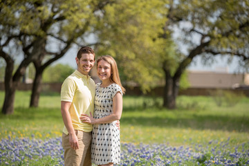 Fototapeta premium Young Millennial Couple Standing During Spring in a Field of Blue Bonnets