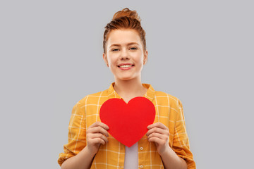 Obraz na płótnie Canvas love, valentine's day and charity concept - smiling red haired teenage girl in checkered shirt with heart over grey background