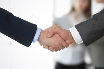 Business people shaking hands at meeting or negotiation, close-up. Group of unknown businessmen and women in modern office at background. Teamwork, partnership and handshake concept