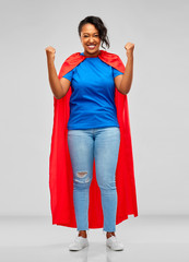 super power and people concept - happy african american young woman in superhero red cape over grey...