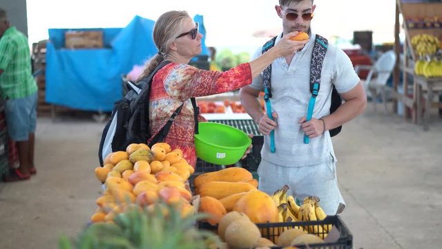 Mature woman picking mangoes at a farmers market and smelling them for freshness.