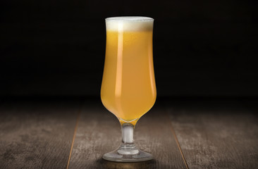Fresh colorful unfiltered New England IPA in stemmed glassware on a wood table against a black...